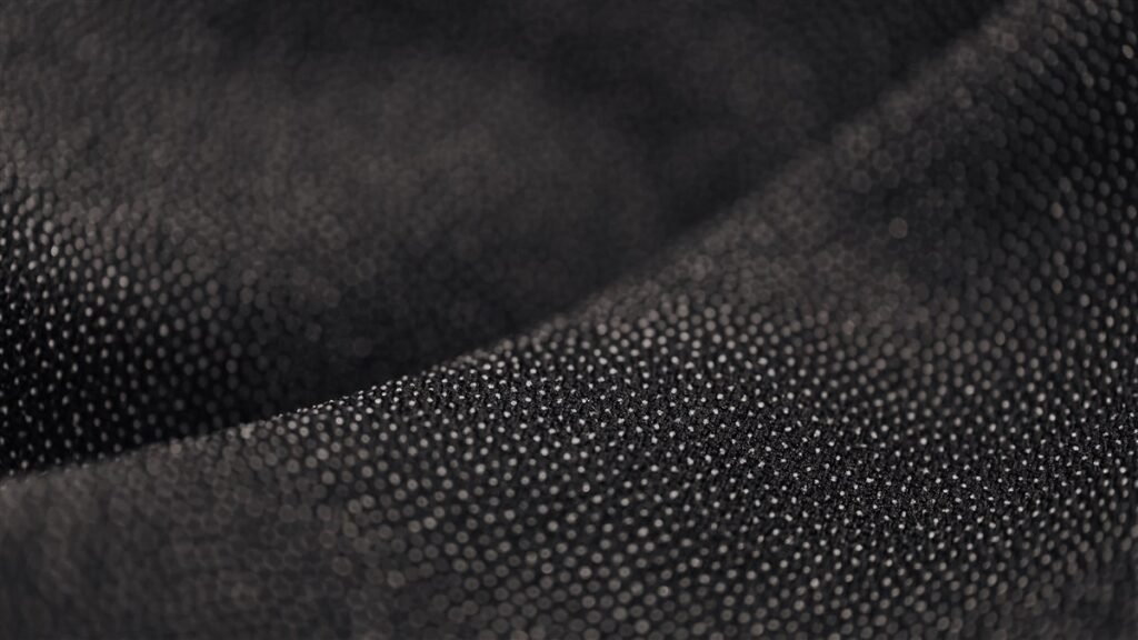 Gros plan sur un textile technique noir à micro-picots, lumière rasante