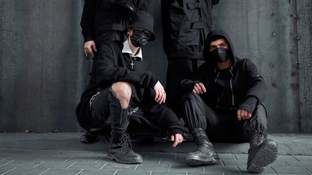 Quatre personnes en tenues techwear noires complètes avec sangles et poches cargo