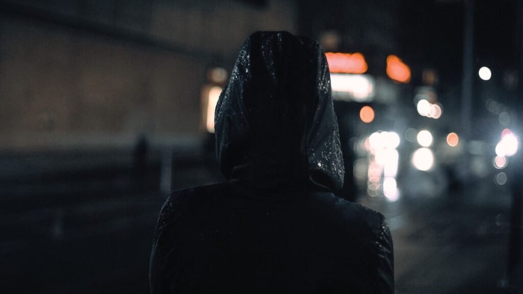 Capuche de veste technique noire couverte de pluie dans une rue la nuit